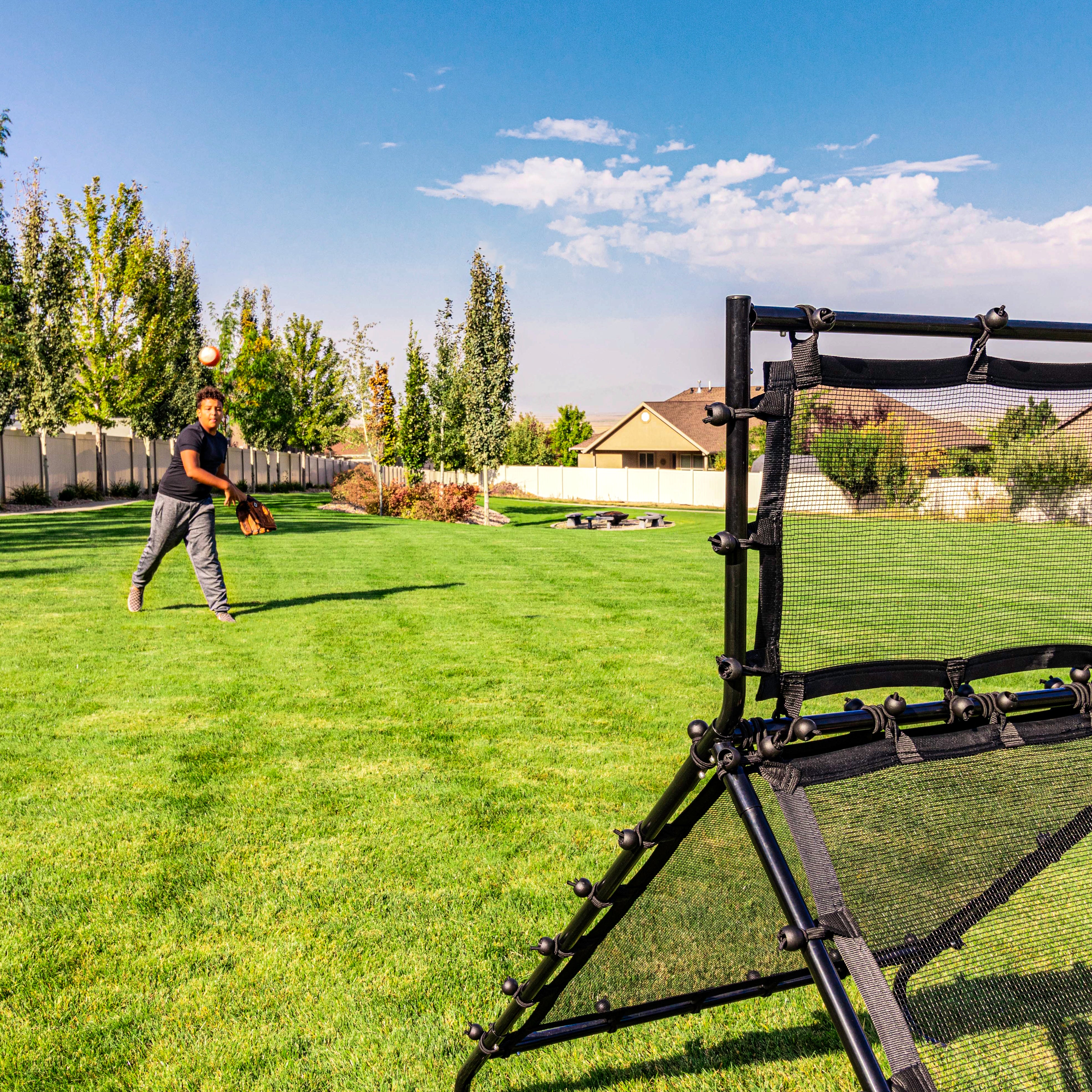 A teenage boy pitching a baseball at the Multi-Sport Training Rebounder. 