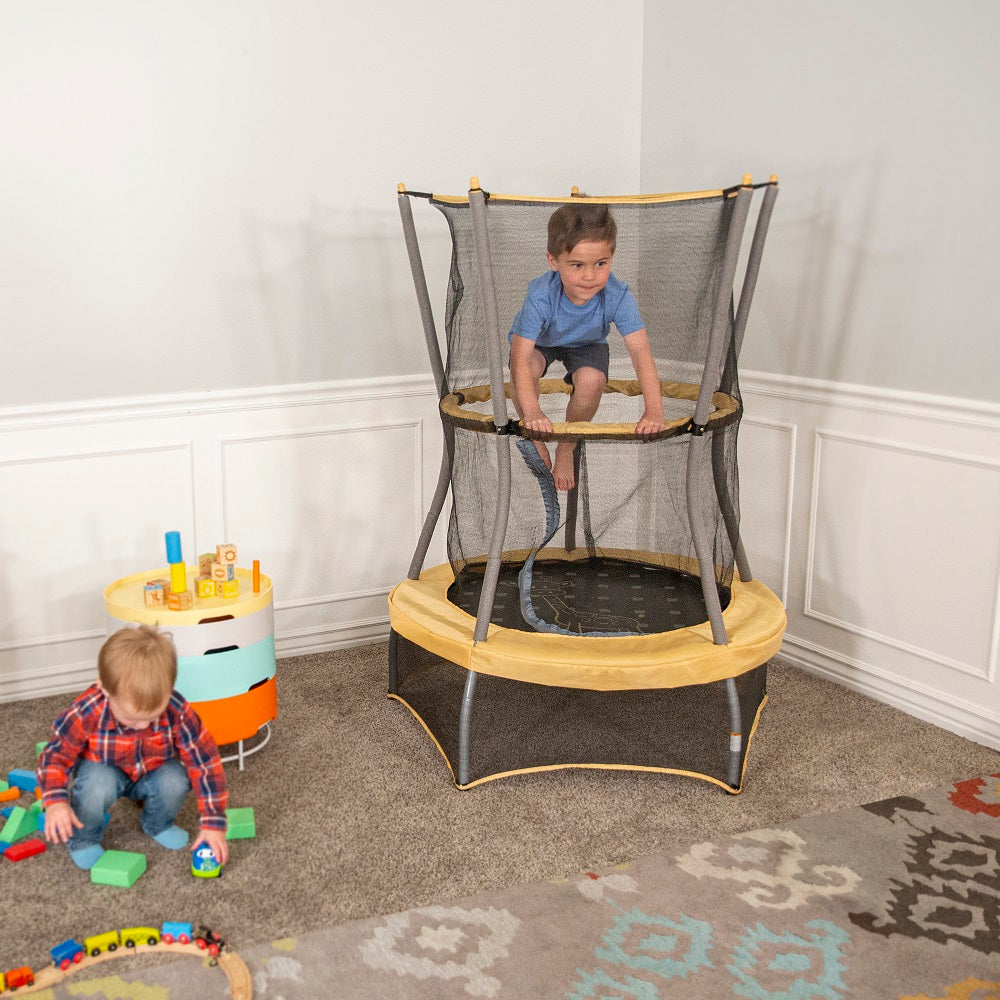 Young boy jumps while holding onto the handlebar. Another young boy plays outside the trampoline. 