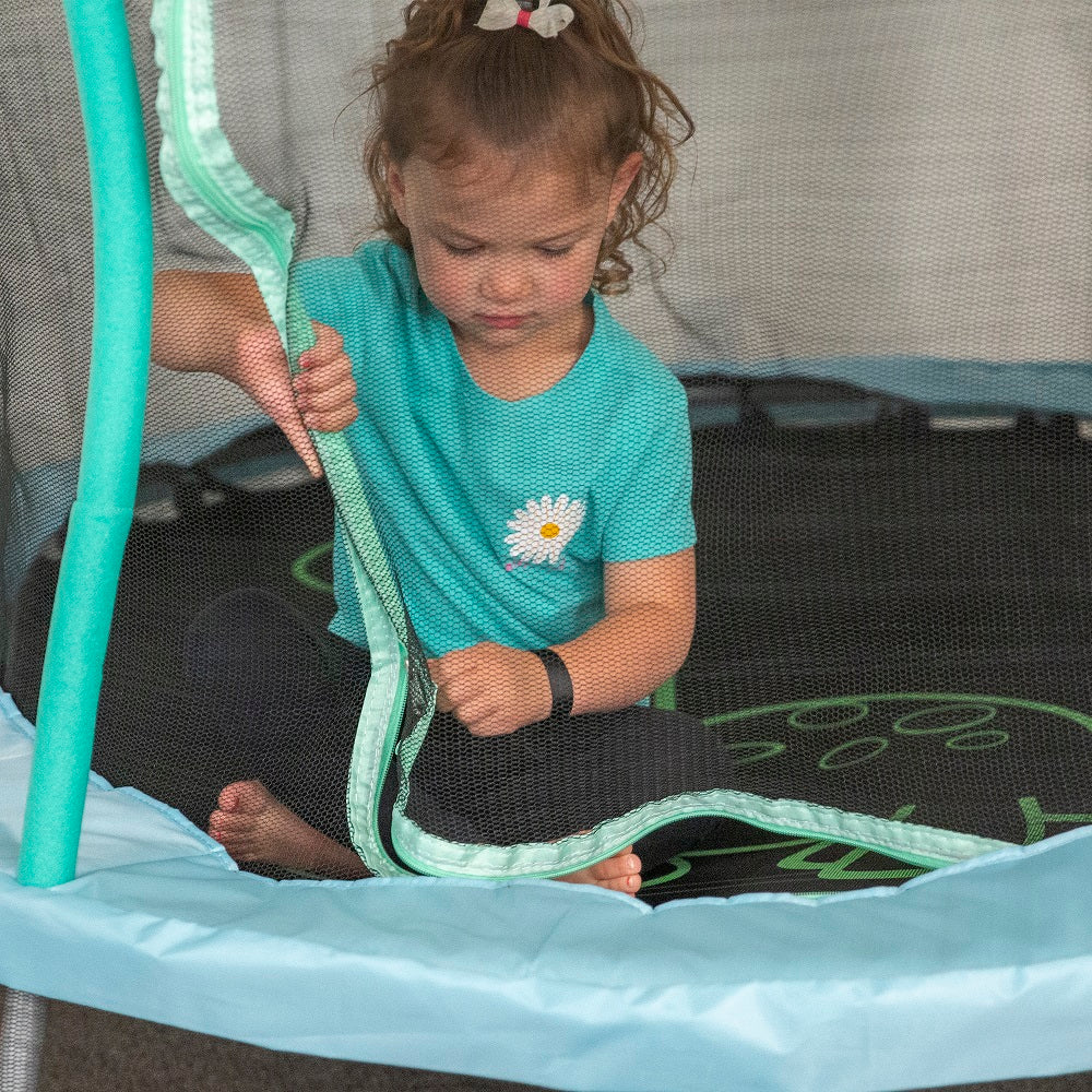 Young girl sits on jump mat while zipping close the enclosure net. 