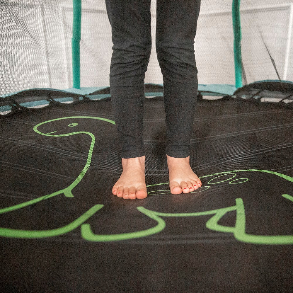 A small girl's legs and feet shown standing on the green dinosaur design. 