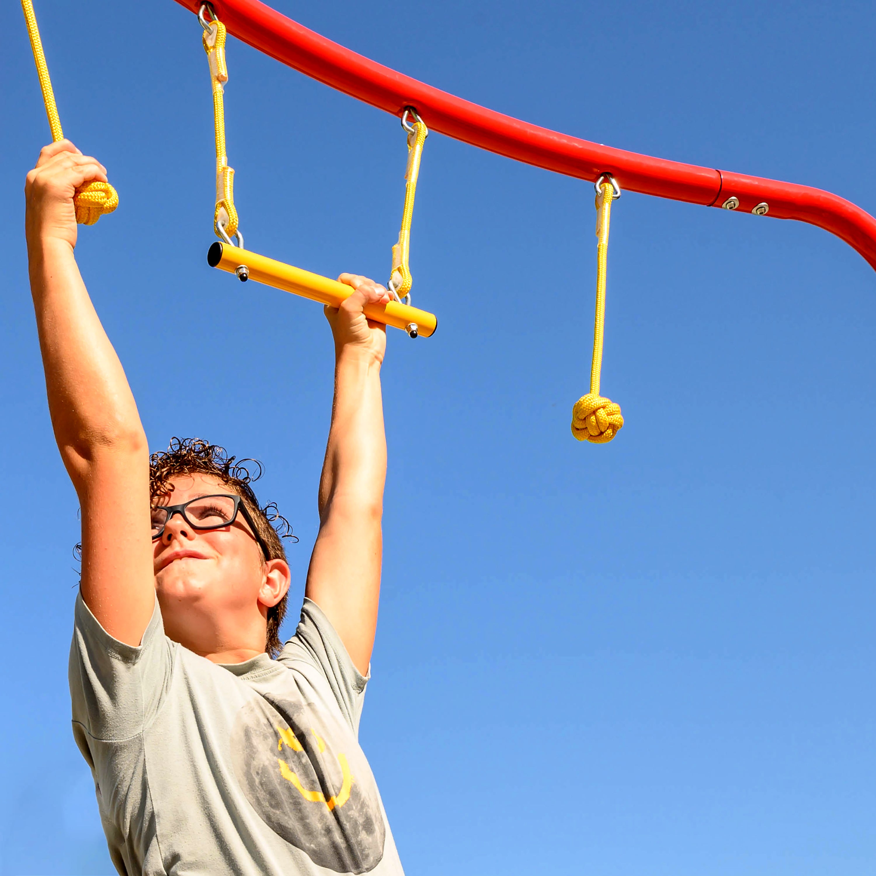 Young boy hangs onto the suspended ninja obstacles on the Hanging Jungle Line. 