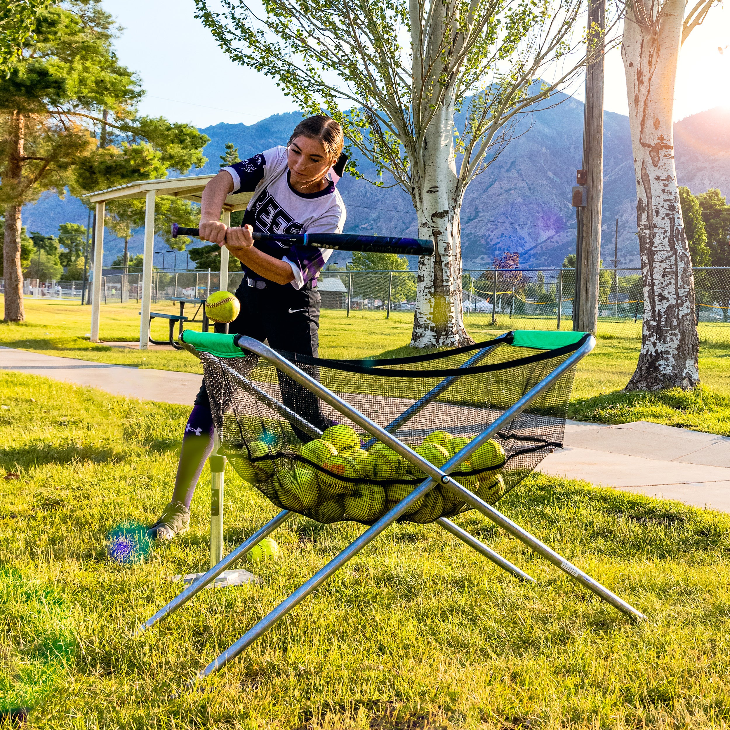 A softball player swings her bat over the folding cart to hit the softball. 